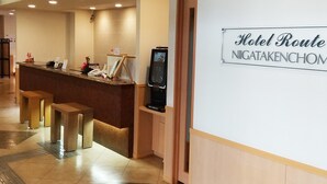 Een hotel receptie met een balie, een bord waarop 'Hotel Route NIGATAKENCHOM' staat en een televisiescherm.