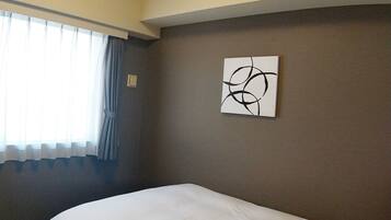 A hotel room with a bed, a window with curtains, and a wall with a piece of abstract art.
