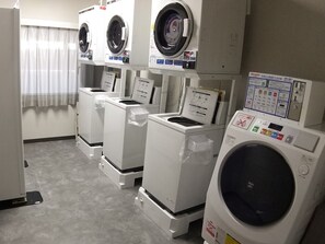 A laundry facility with multiple washing machines and dryers, a control panel, and a window with curtains. - Hotel Route-Inn Niigatakencho Minami (Niigata)