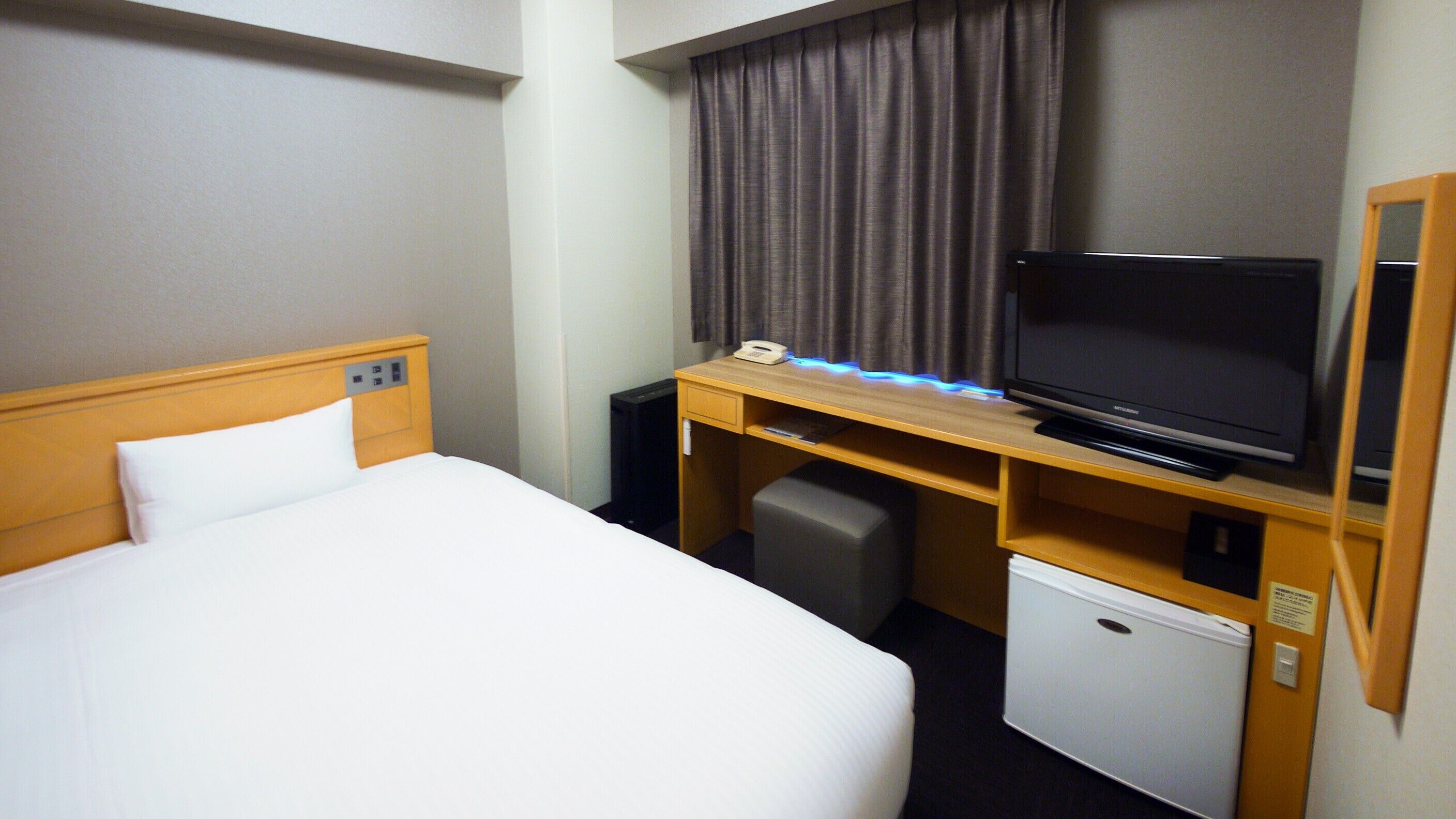 Una habitación de hotel con una cama, un escritorio con televisor, un refrigerador pequeño y un teléfono.