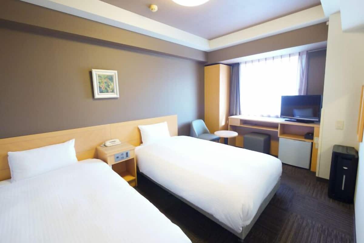 A hotel room with two beds, a desk with a TV, a small table, and a chair.
