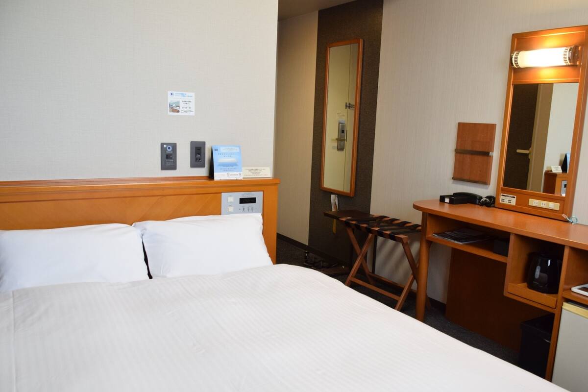 A hotel room with a large bed, a desk with a mirror, and a small kitchenette.