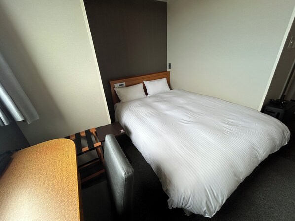 A hotel room with a single bed, a wooden nightstand, a chair, and a small table.