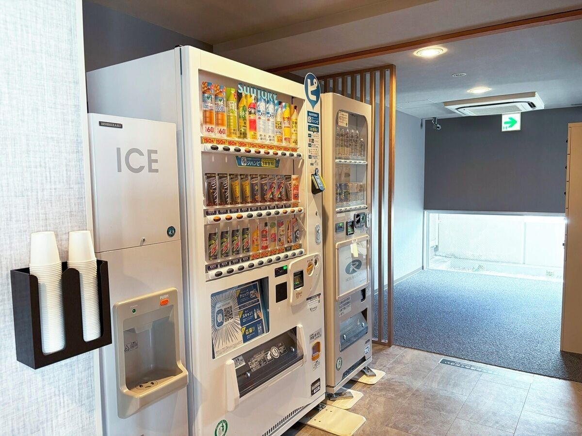 Una máquina expendedora con varias bebidas y aperitivos, un dispensador de agua y un bote de basura.