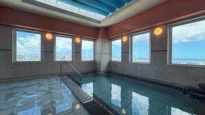 En rymlig inomhuspool med stora fönster som erbjuder utsikt över staden och havet.