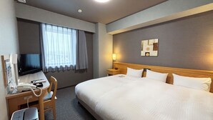 Ett hotellrum med en stor säng, ett skrivbord med en dator och en telefon, en tv och ett fönster med gardiner.