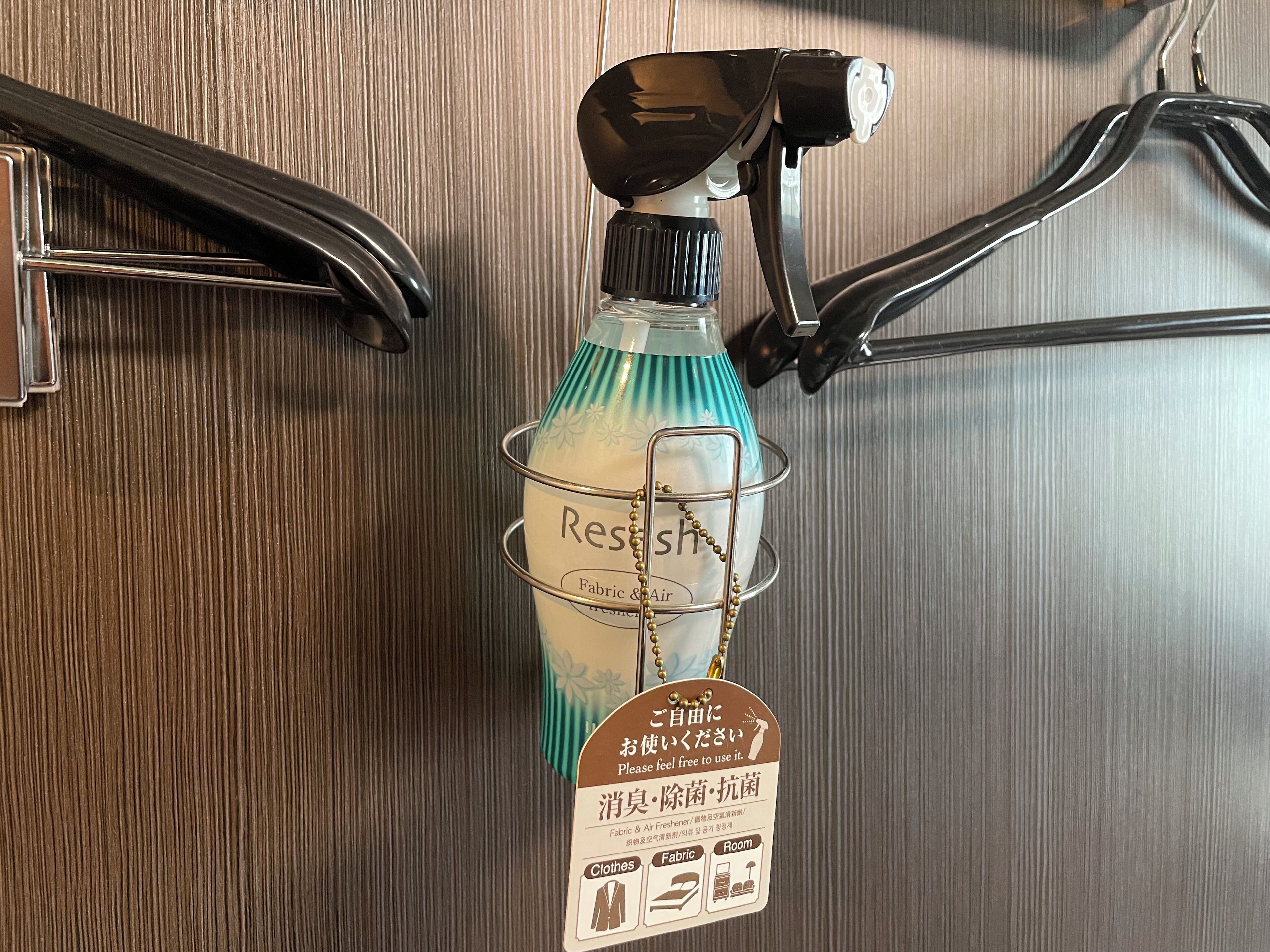 Una botella de aromatizante de tela y ambiente, etiquetada como "Resh", con una etiqueta que incluye texto japonés e iconos de ropa y tejidos.