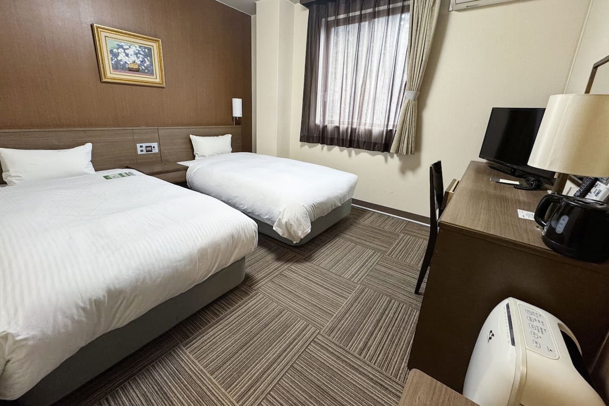 Habitació d'hotel amb dos llits, televisió, cafetera i finestra amb cortines.