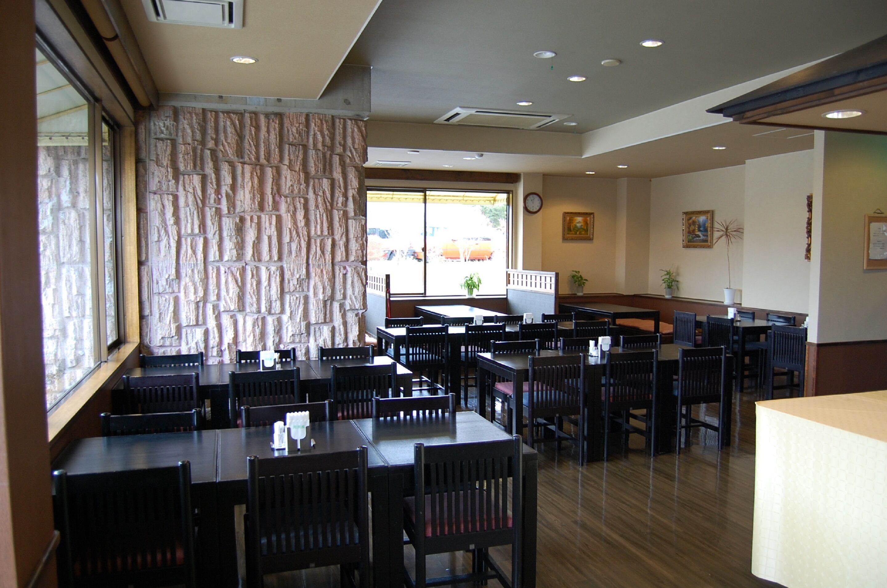 A restaurant with multiple tables and chairs, a stone wall, and a view of the outside.