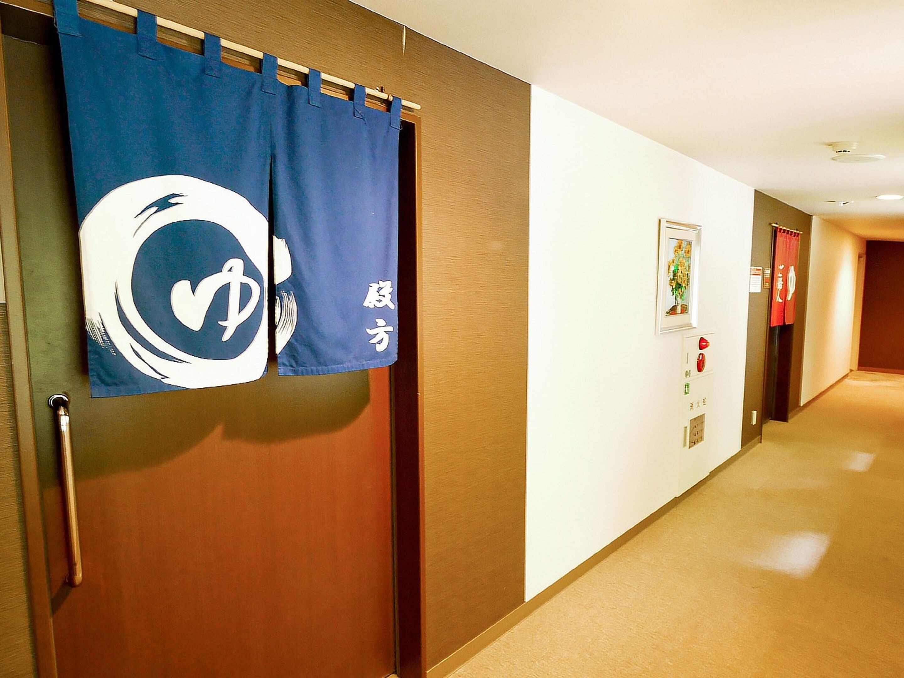 Un couloir d’hôtel avec une porte en bois, un rideau bleu orné d’un logo et un rideau rouge.