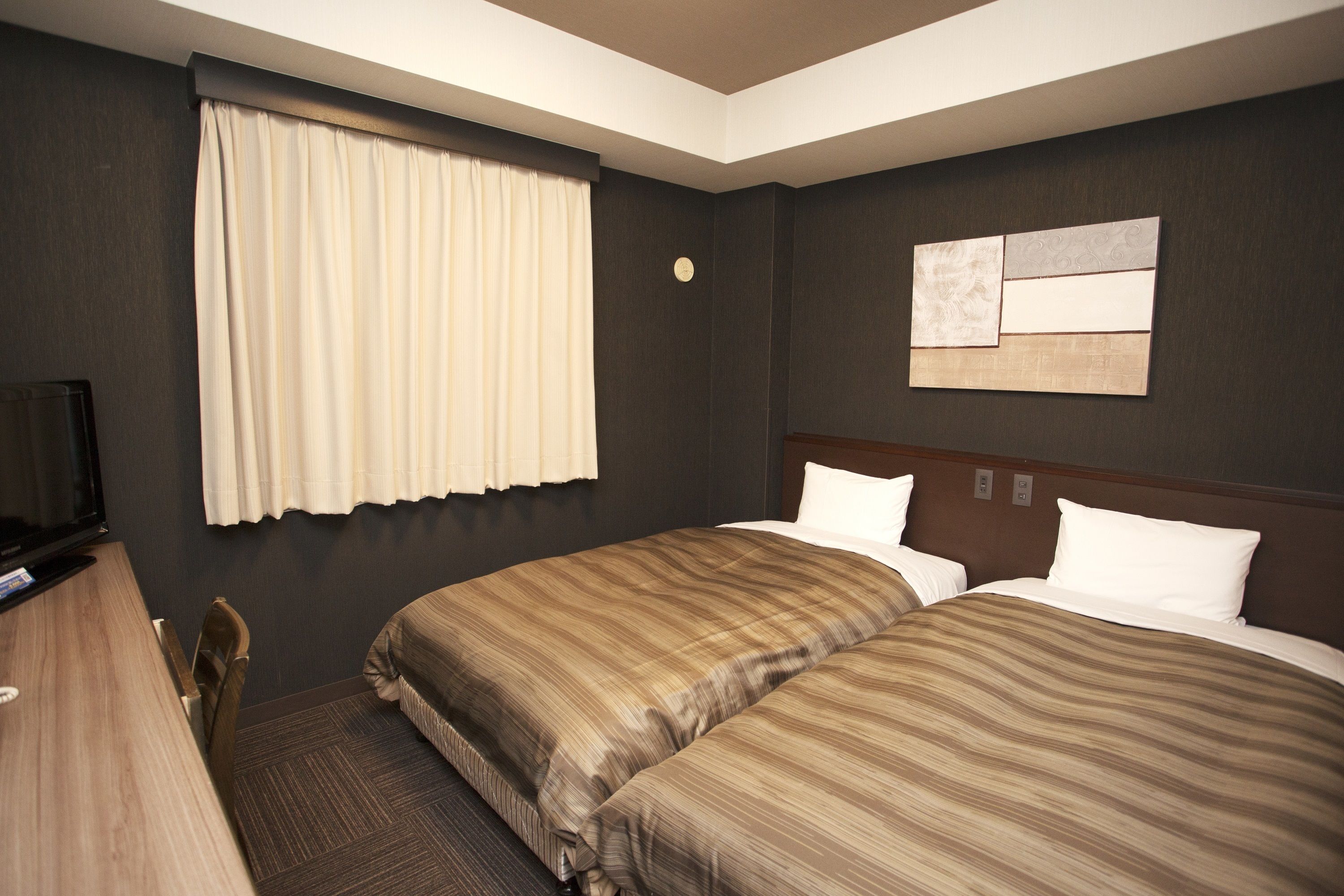 Una habitación de hotel con dos camas, un escritorio, un televisor y una ventana con cortinas.