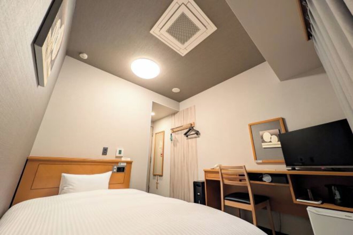 A hotel room with a bed, desk, chair, and a television.
