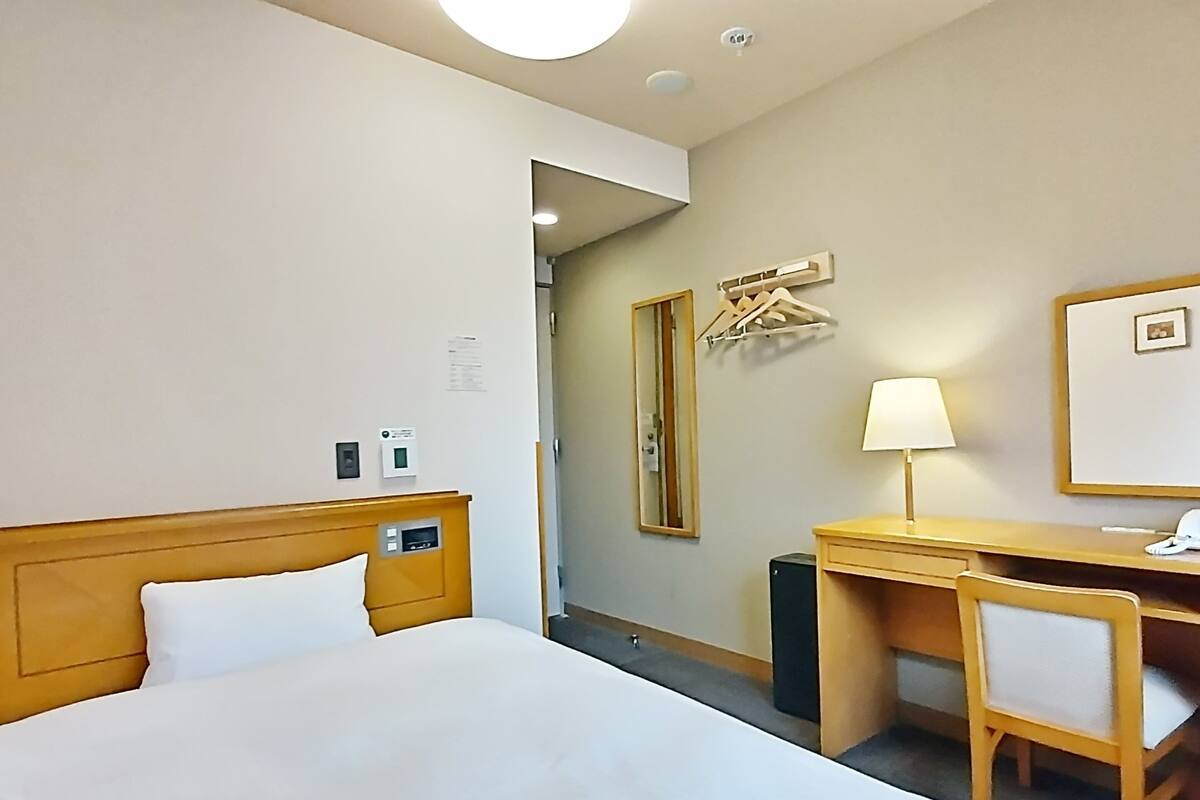 Ein Hotelzimmer mit Bett, Schreibtisch, Stuhl, Spiegel, Lampe und Kleiderhaken.