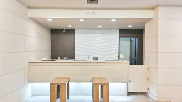 A reception area with a counter, two wooden stools, a wall-mounted sign, and a door. - Hotel Route-Inn Aomori Ekimae (Aomori)