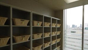 A room with a large window, a white wall, and shelves with baskets. - Hotel Route Inn Osaka Honmachi (Osaka)