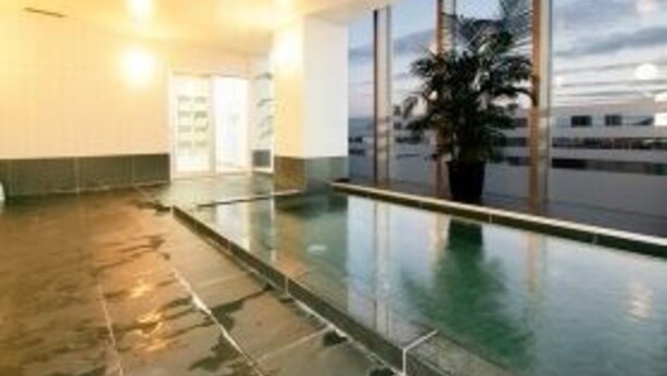 A hotel lobby with a large indoor pool, a palm tree, and a view of the sea. - Hotel Route Inn Osaka Honmachi (Osaka)
