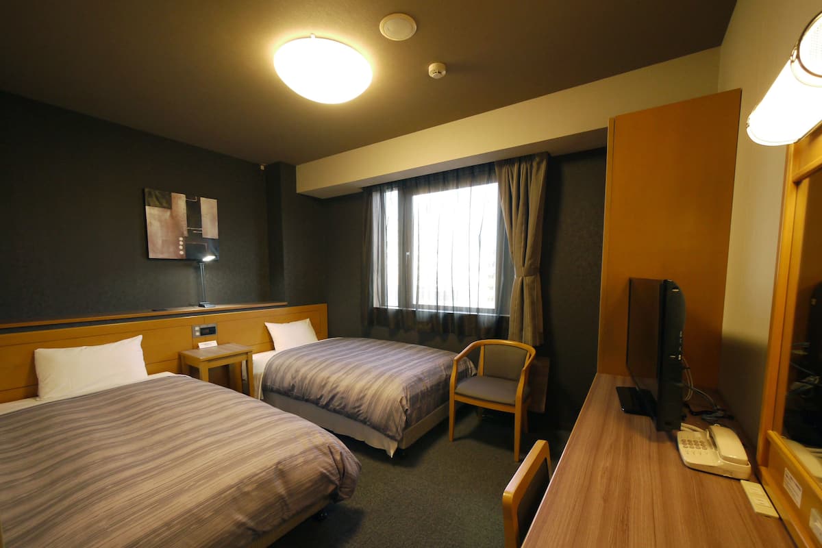 A hotel room with two beds, a desk, a chair, a television, and a telephone.