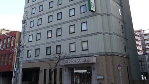 A multi-story hotel with a modern design, featuring a prominent green sign on the facade and a clear entrance with a glass door. - Hotel Route Inn Sapporo Kitayojo (Sapporo)