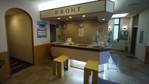A reception area with a 'FRONT' sign, a clock, and a fire extinguisher. There are two wooden stools and a counter with informational brochures. - Hotel Route Inn Sapporo Kitayojo (Sapporo)