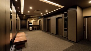 A hotel corridor with a bench, multiple elevators, and a carpeted floor. - Hotel Route-Inn Grand Tokyo Toyocho (Tokyo)