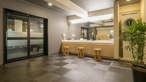 Ein modernes Hotelbad mit Schachbrettboden, einem großen Spiegel und einer Topfpflanze.