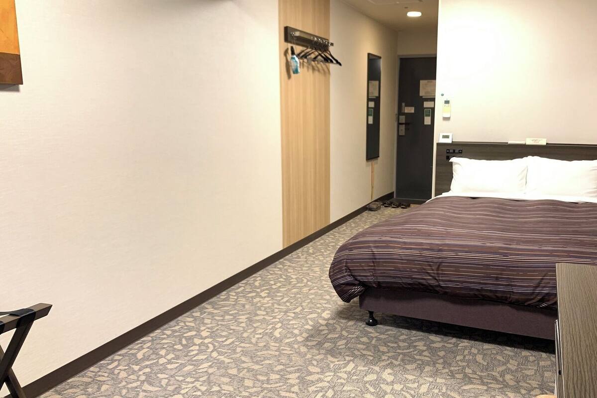 Ein Hotelzimmer mit Bett, Schreibtisch, Schuhablage und Tür.