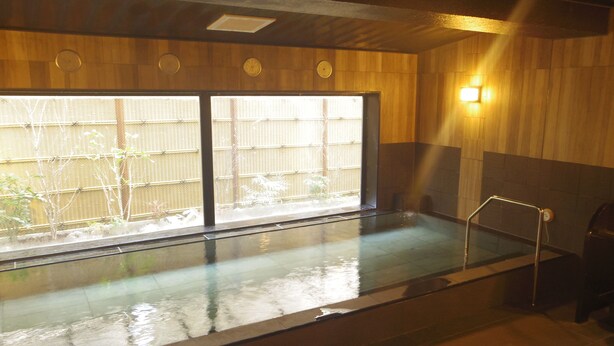 Ein traditionelles japanisches Onsen mit Holzeinrichtung, einem in Glas eingeschlossenen Thermalbad und Blick auf Bambus.