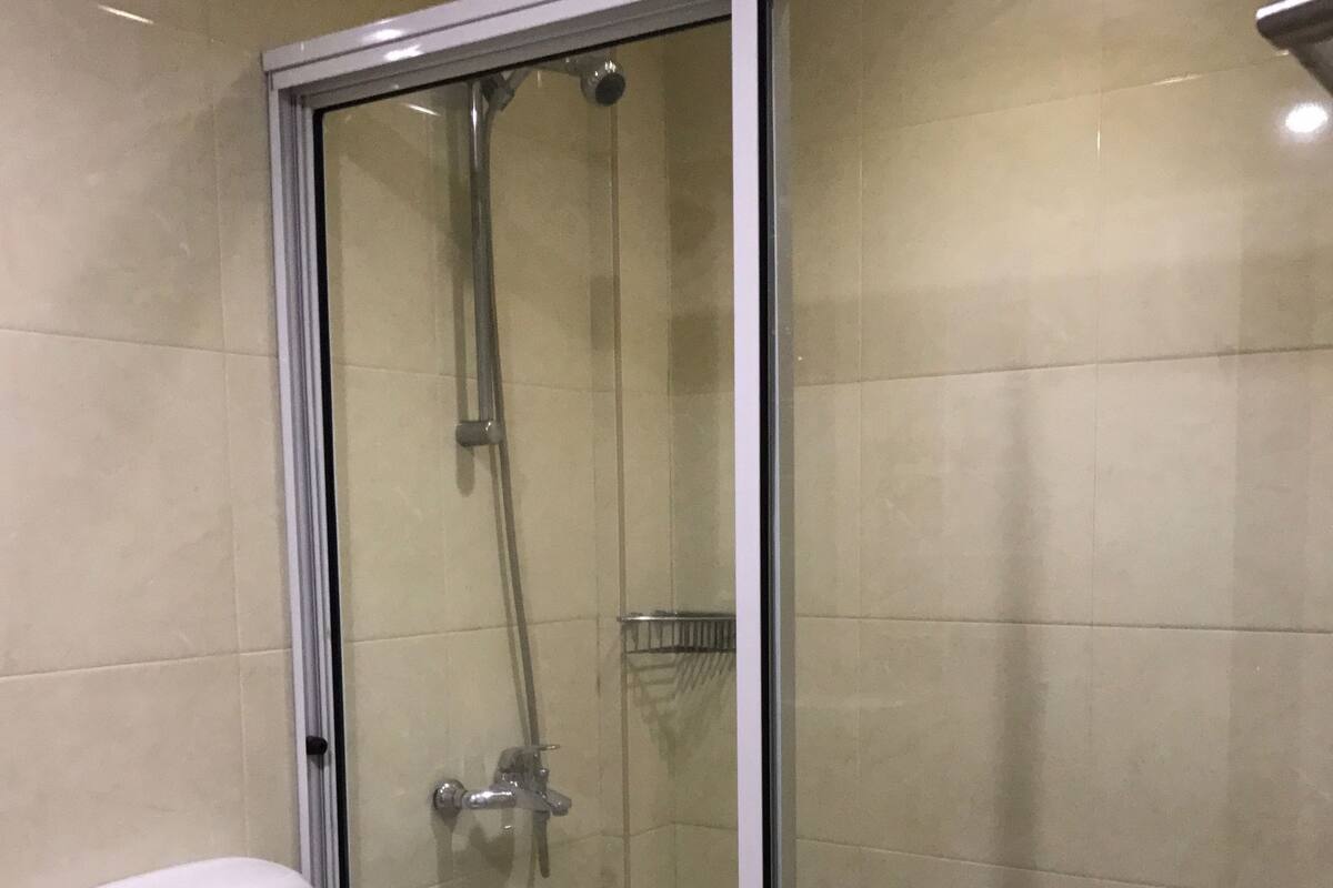 A bathroom with a glass-enclosed shower, a white toilet, and beige tiled walls.