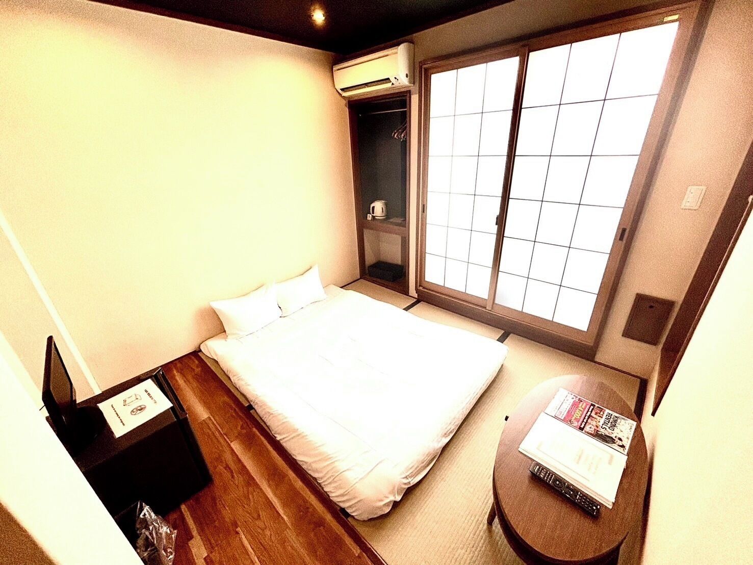 Una habitación de hotel con cama, una mesita con revistas, armario y un ventanal grande.