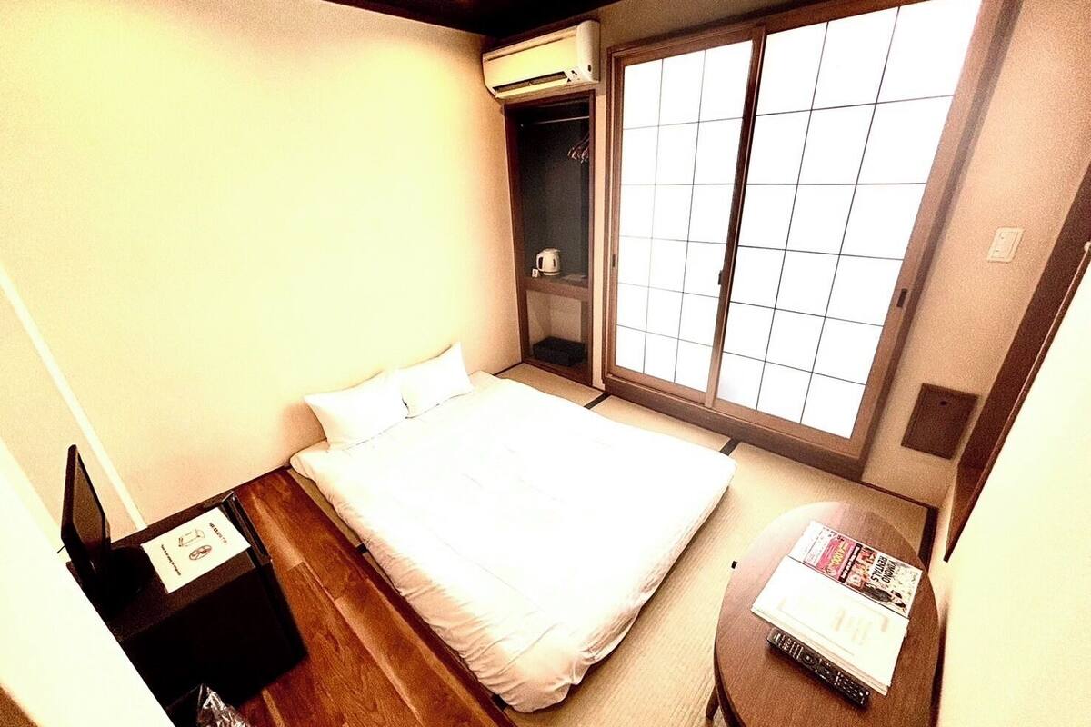 A hotel room with a bed, a small table with magazines, a wardrobe, and a large window.