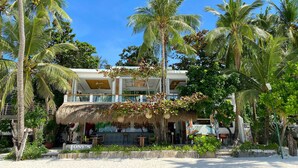 Une propriété située en bord de mer, dotée d’un bar à toit de chaume, de sièges en plein air et de palmiers.