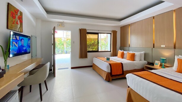 Una habitación de hotel con cama, escritorio, televisor y ventana con cortinas.