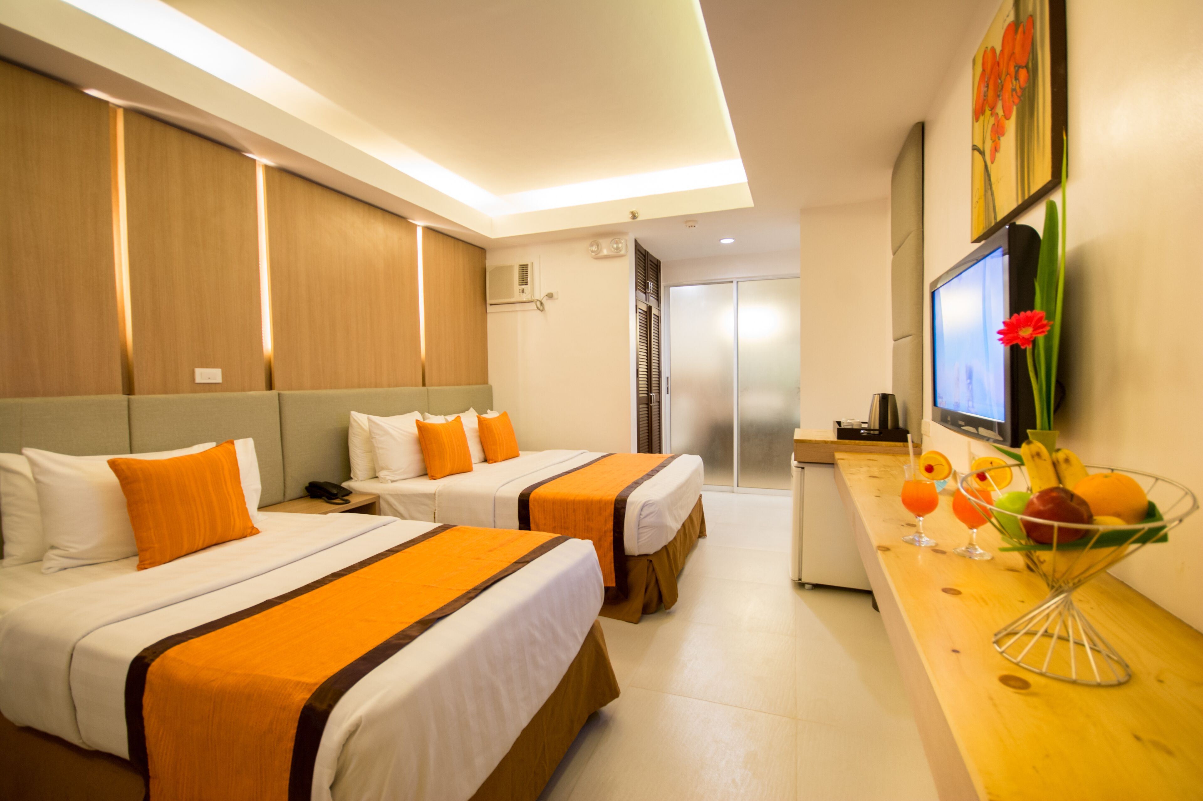 Ein Hotelzimmer mit zwei Betten, einem Schreibtisch mit Computer und einer Obstschale sowie einem Fernseher an der Wand.