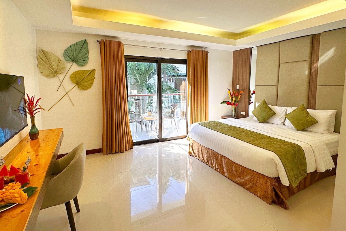 Una habitación de hotel con cama, televisión, mesa de comedor con comida y balcón con plantas.