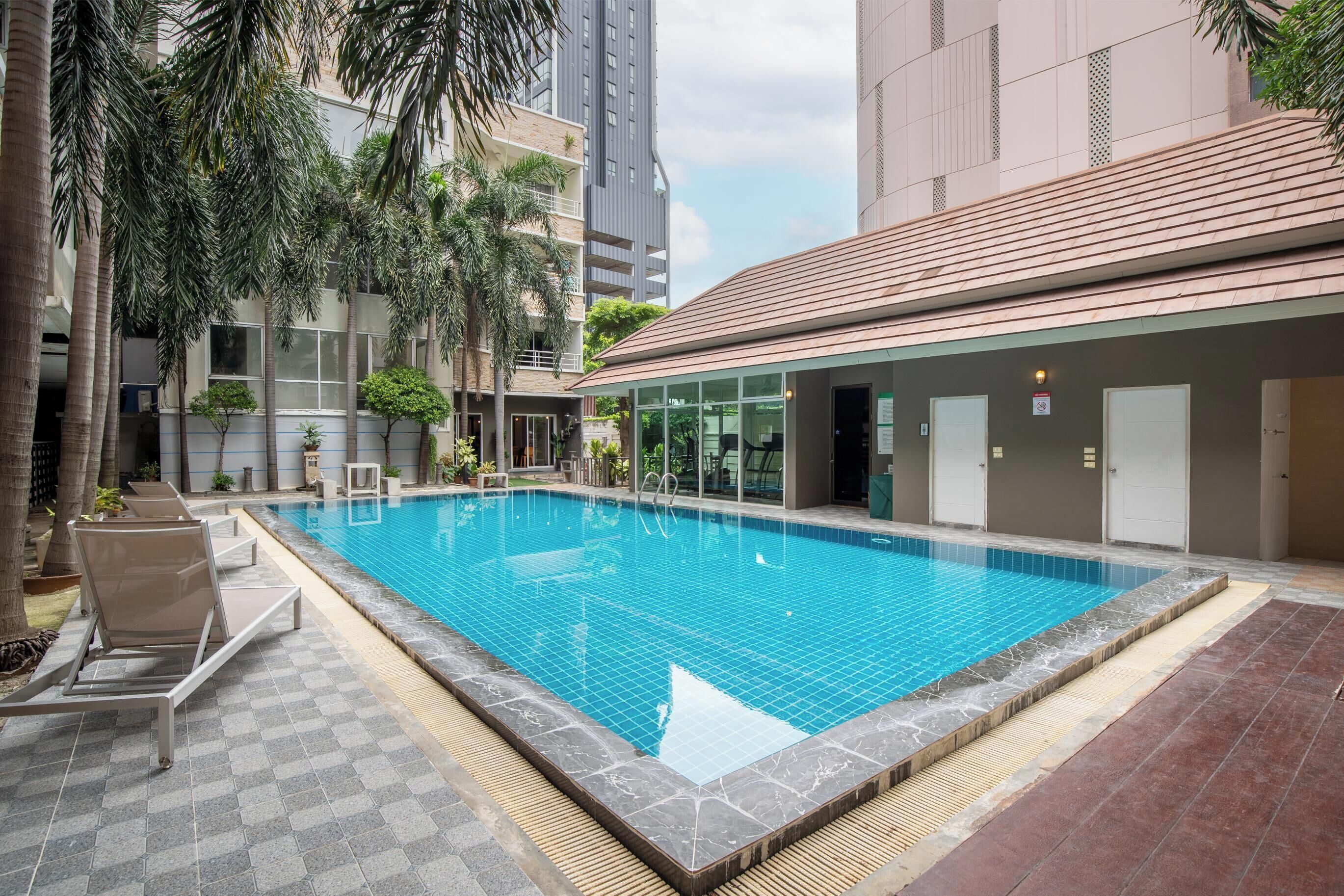 A swimming pool with lounge chairs, surrounded by palm trees and modern buildings.