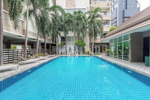 A swimming pool with tiled blue floor, surrounded by lounge chairs and palm trees, with buildings in the background. - P-Park Suvarnabhumi (Bangkok)