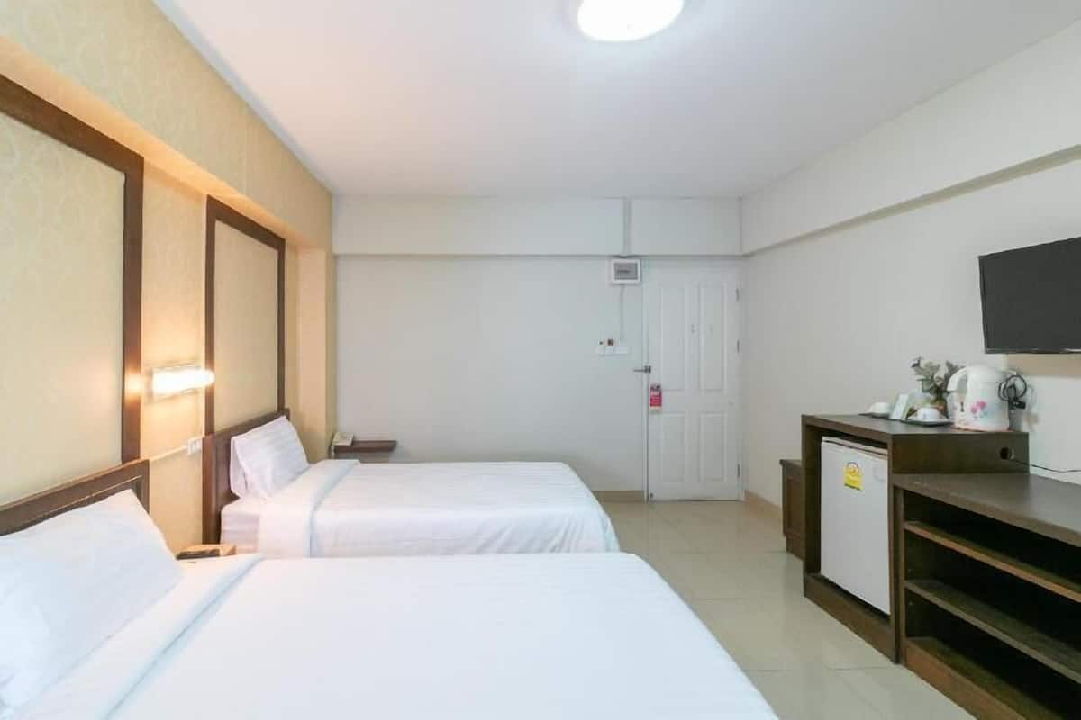 Ein Hotelzimmer mit zwei Betten, einem Fernseher, einer kleinen Kühlbox und einer Tür.