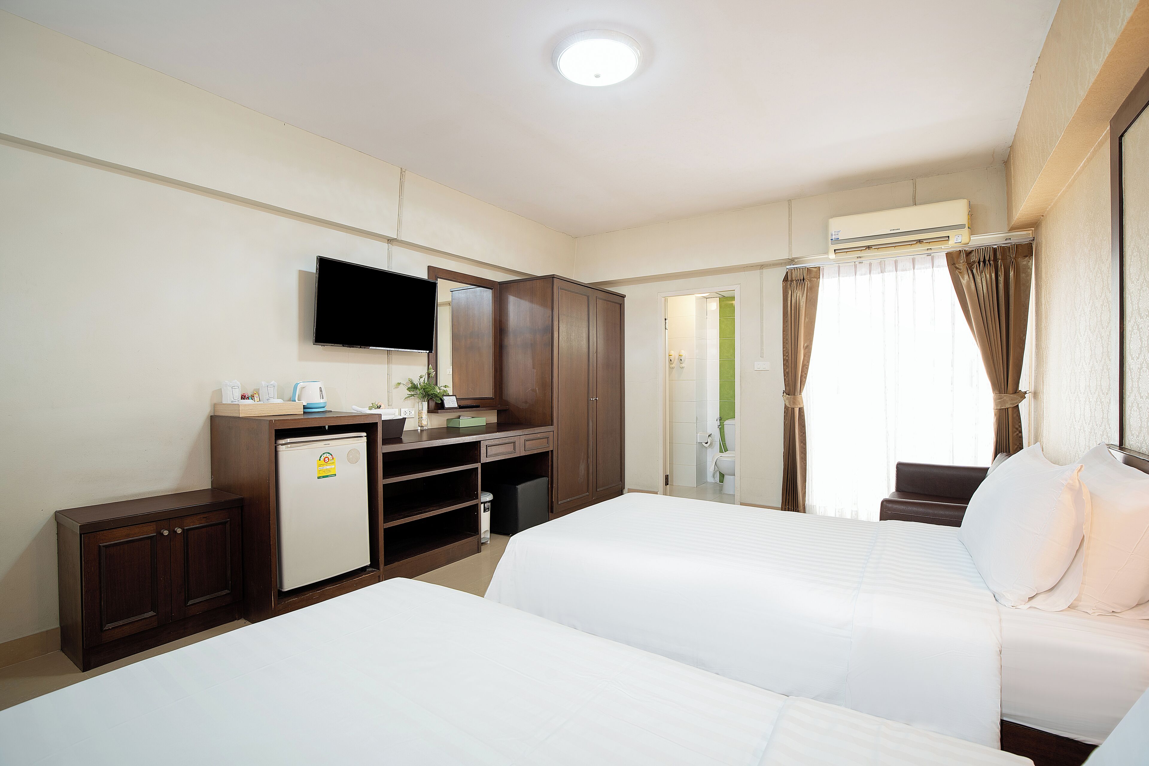 A hotel room with two beds, a desk with a computer, a television, and an air conditioning unit.