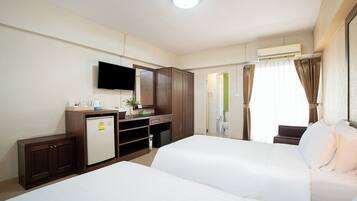 A hotel room with two beds, a desk with a computer, a television, and an air conditioning unit.