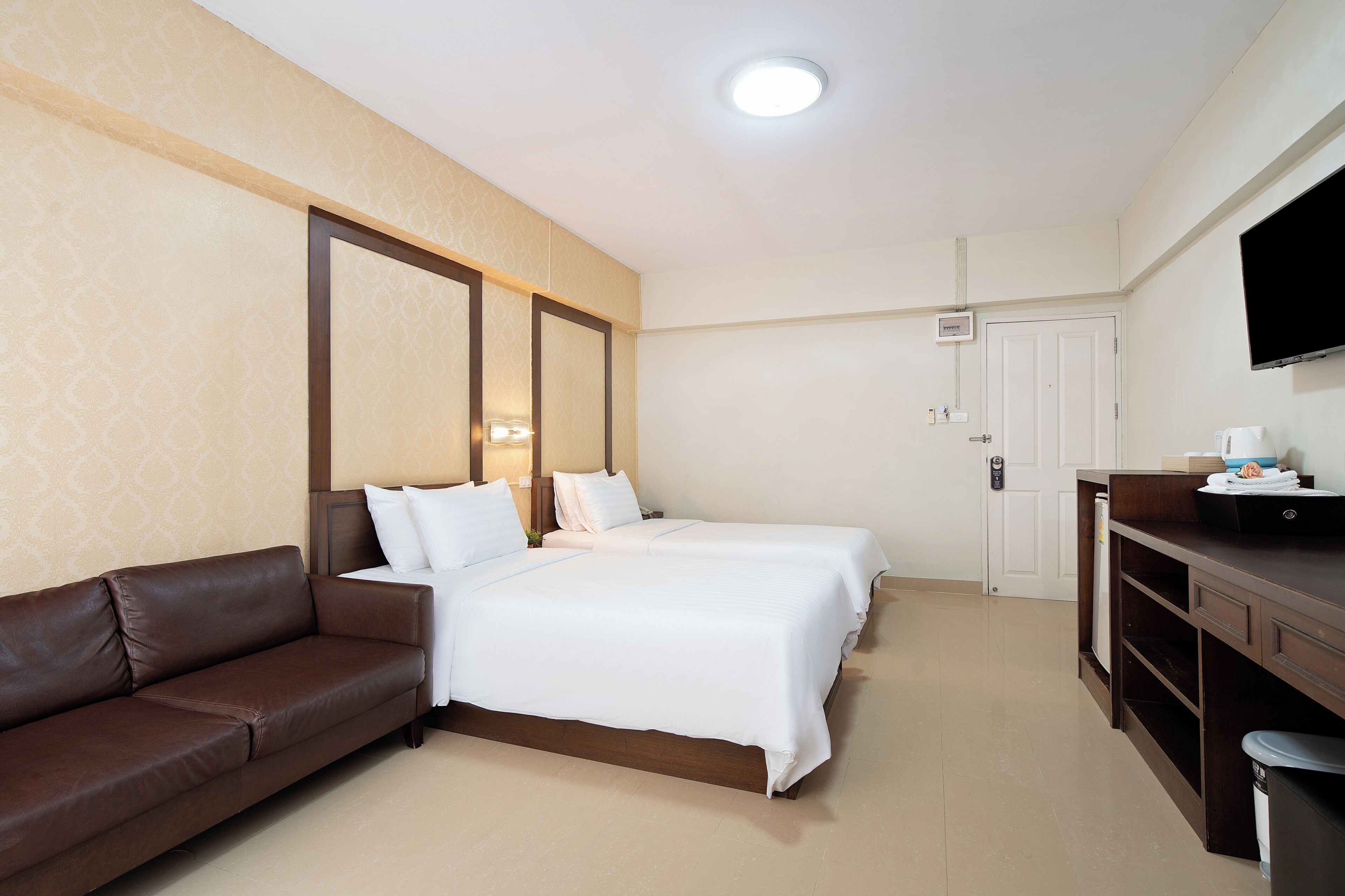 Une chambre d’hôtel avec un lit, un canapé marron, une télévision et un bureau avec un ordinateur.