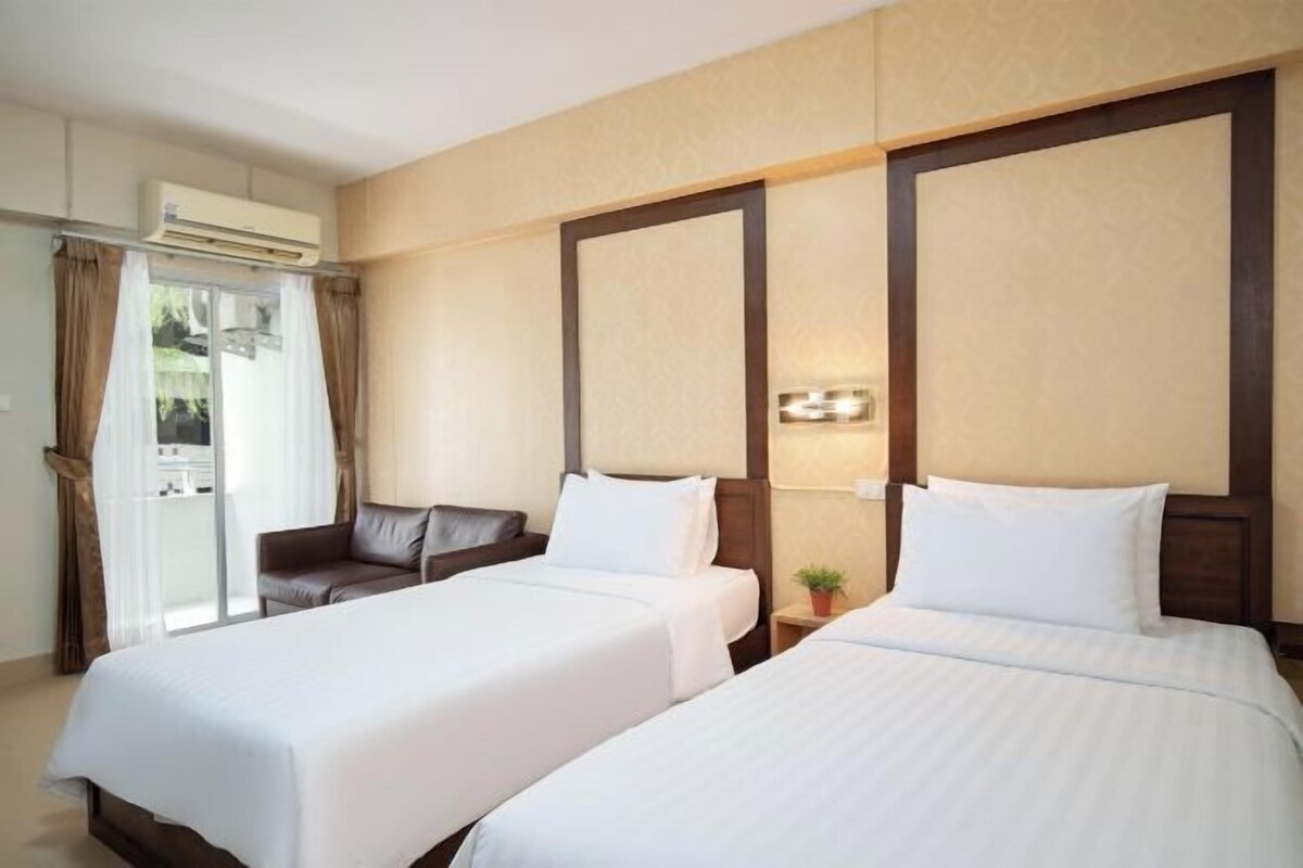 A hotel room with two beds, a sofa, an air conditioning unit, and a window with curtains.