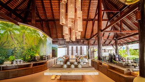 Un área de bar espaciosa y moderna, con techo alto, vigas de madera y un mural tropical en la pared.