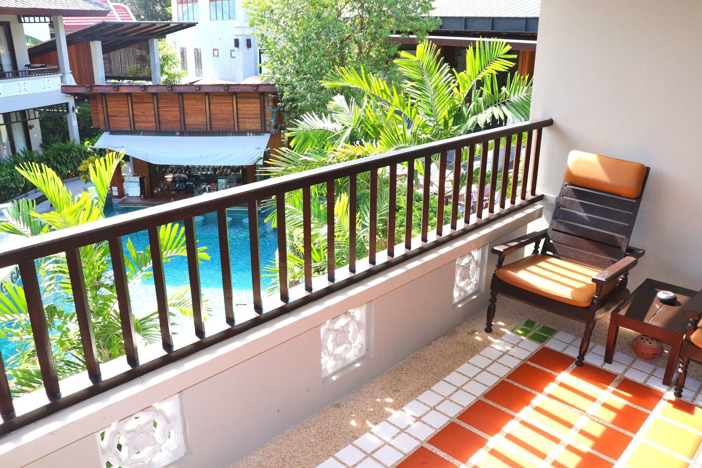Un balcón con piscina, mobiliario de madera y plantas tropicales.