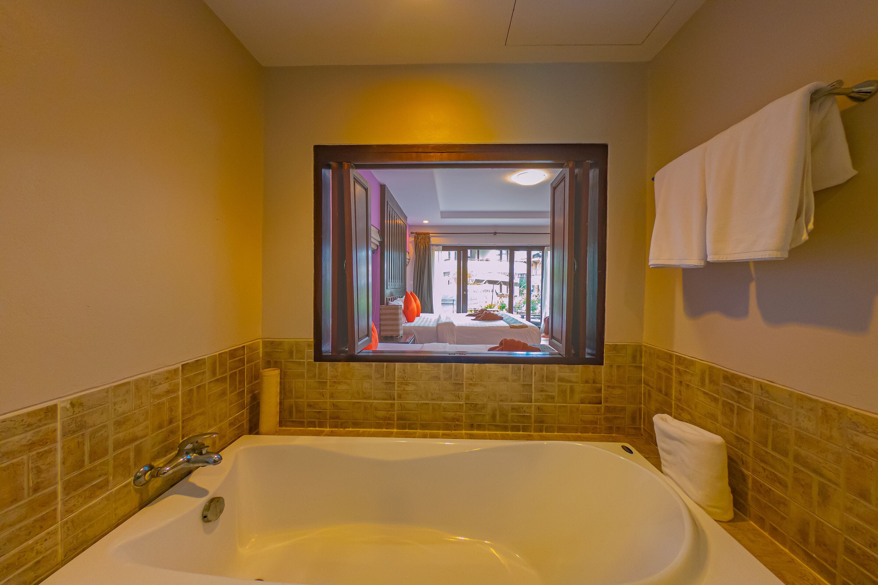 Un baño con una bañera grande, un ventanal con vista a una habitación y un perchero para toallas.
