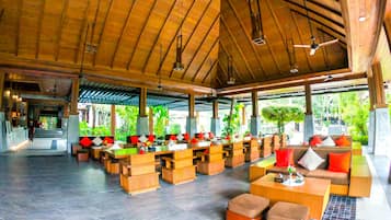A spacious indoor area with wooden ceiling beams, multiple seating arrangements, and large windows allowing natural light.