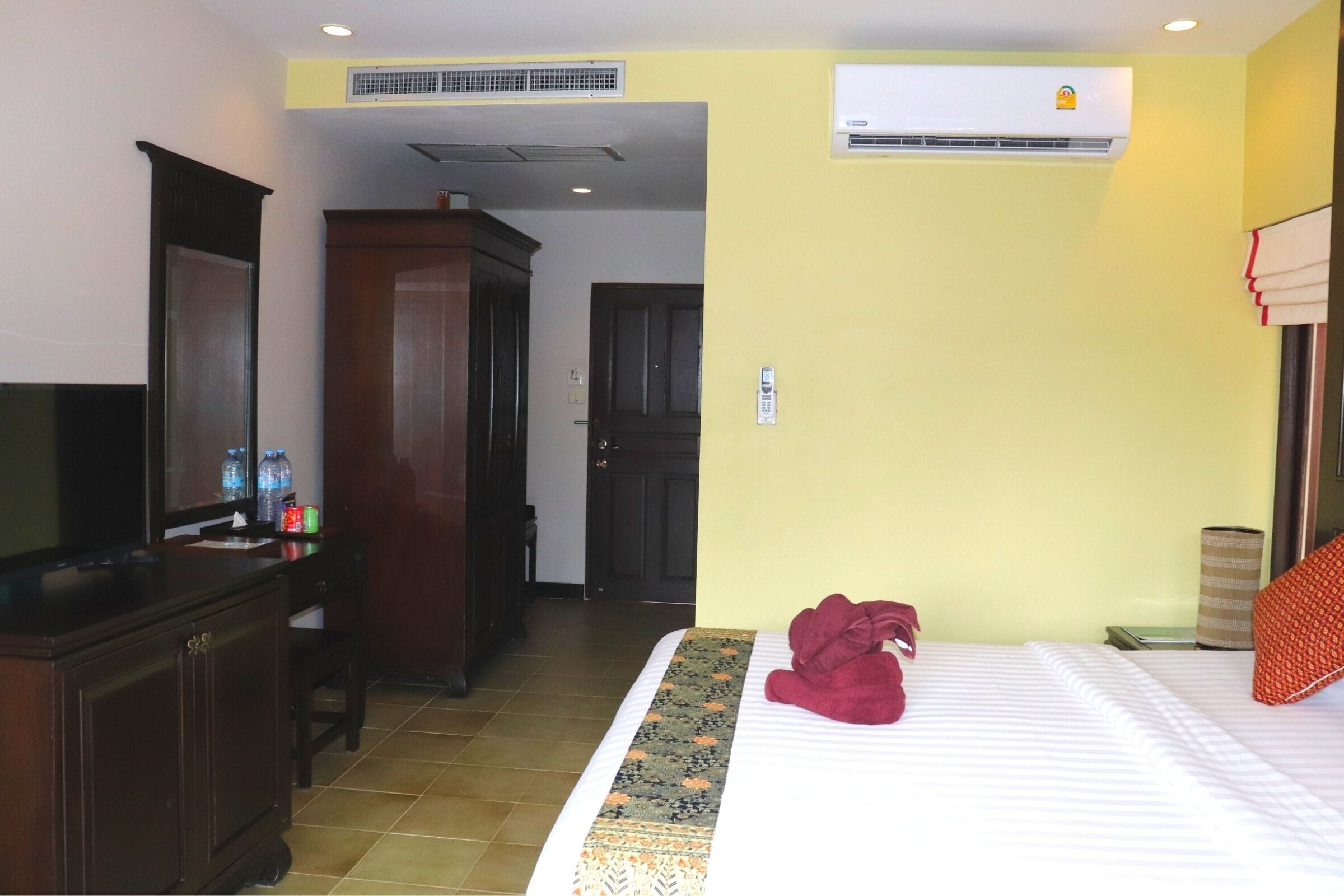 A hotel room with a bed, a desk, a television, and an air conditioning unit.