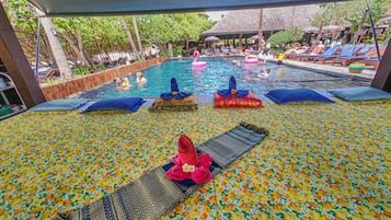 Relax by the pool surrounded by lush greenery and vibrant flowers, with lounge chairs and a shaded seating area.