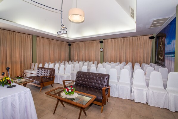 A conference room with a stage, white chairs, a brown sofa, and a table with flowers. - Chaweng Garden Beach Resort (Koh Samui)