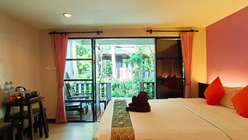 Hotellihuone, jossa on sänky, työpöytä tuolilla, pöytä ja näkymä puutarhaan liukuoven kautta.