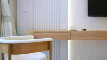A modern room with a wooden desk, a white chair, a flat-screen TV mounted on the wall, and a window with vertical blinds.